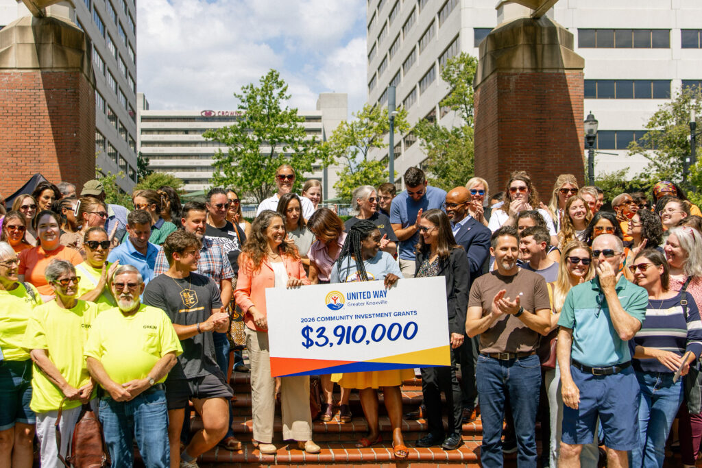 Knoxville Mayor Indya Kincannon (left) and Chrystal Armstrong Brown, President and CEO of United Way of Greater Knoxville (right), stand at the center of a large crowd on brick steps in downtown Knoxville, holding an oversized check that reads "United Way Greater Knoxville, 2026 Community Investment Grants, $3,910,000." People around them are smiling and clapping on a sunny day, with office buildings and trees in the background.